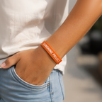 Person wearing an orange 'Sunshine Project' wristband with a blurred background